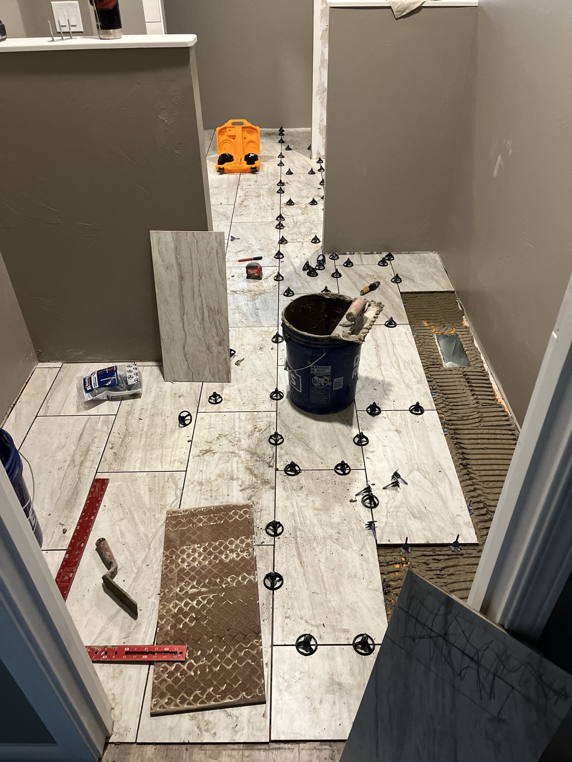 Large-format bathroom floor tile being set and leveled