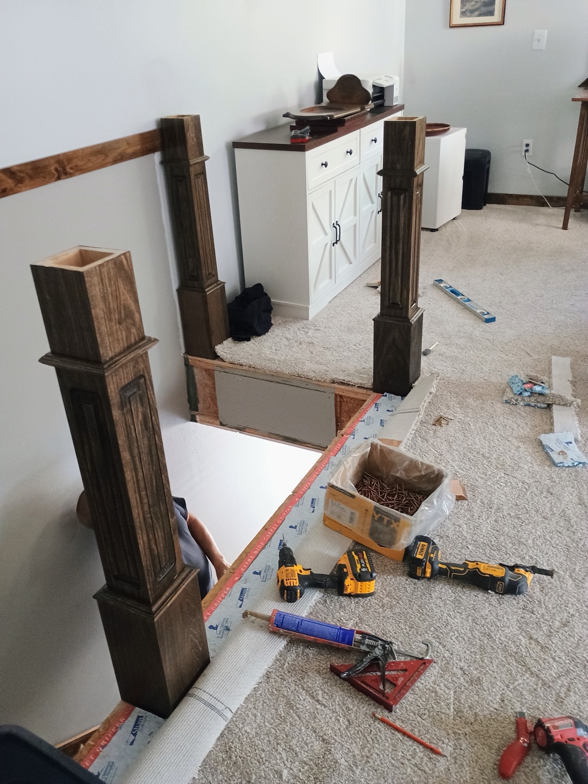 Custom dark-stained newel posts being installed around the stair opening