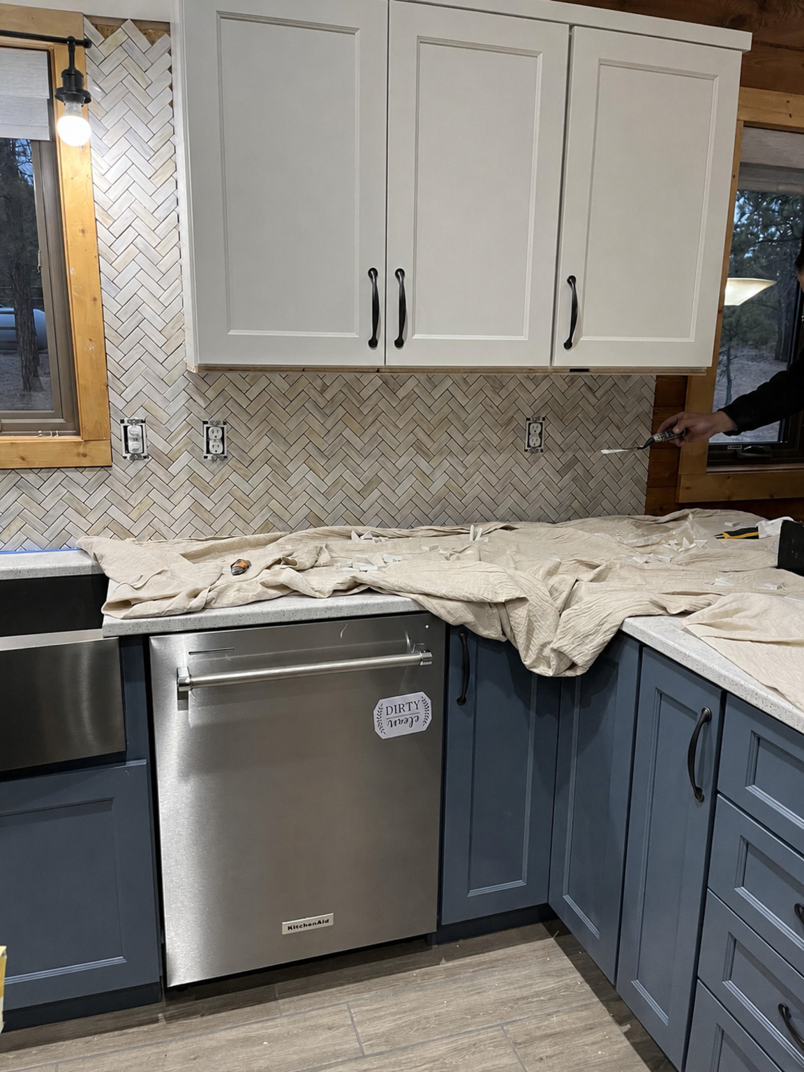 Herringbone tile backsplash aligned beneath white cabinets and around kitchen outlets