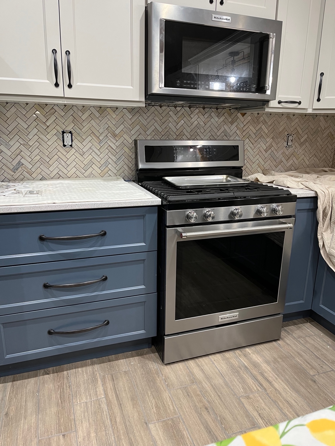 Herringbone tile backsplash installed behind a stainless steel range and microwave