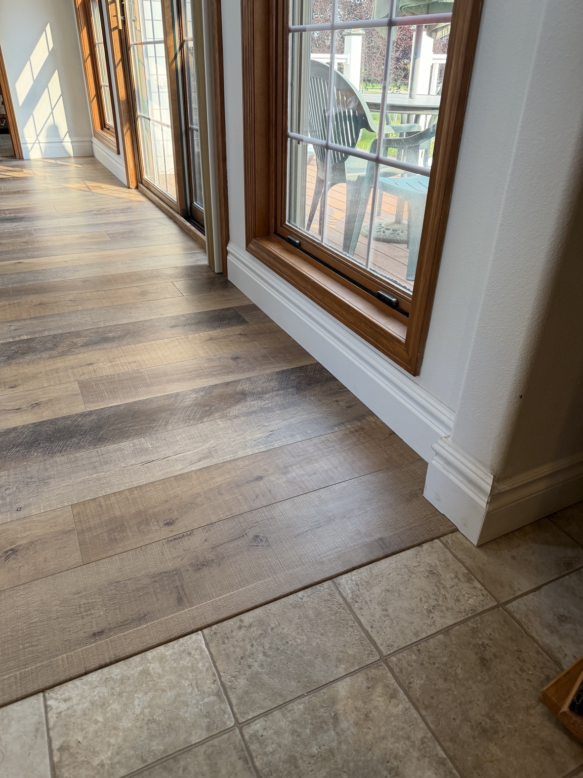 Finished laminate floor and custom white baseboard below wood-trimmed windows